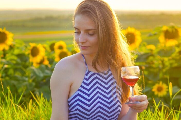 Bella mujer sosteniendo una copa de vino en medio del jardín de girasoles