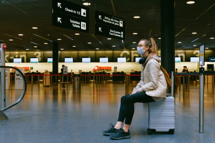 Chica sentada en su equipaje en el aeropuerto y con una máscara