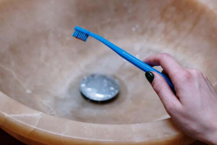 sosteniendo un cepillo de dientes azul frente a un fregadero marrón